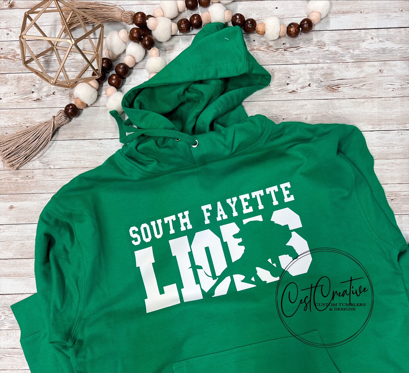 Kelly green hooded sweatshirt with white text. South Fayette over LIONS. Image of a lion is knocked out of the word lion for an artistic effect.